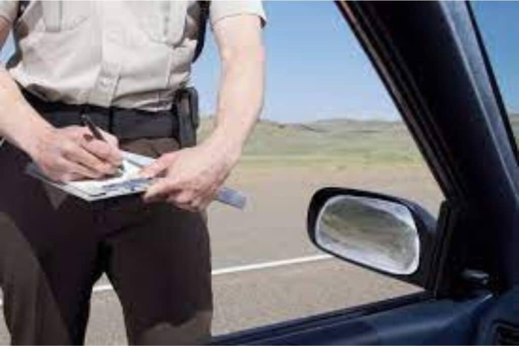Policial escrevendo multa ao lado de carro.